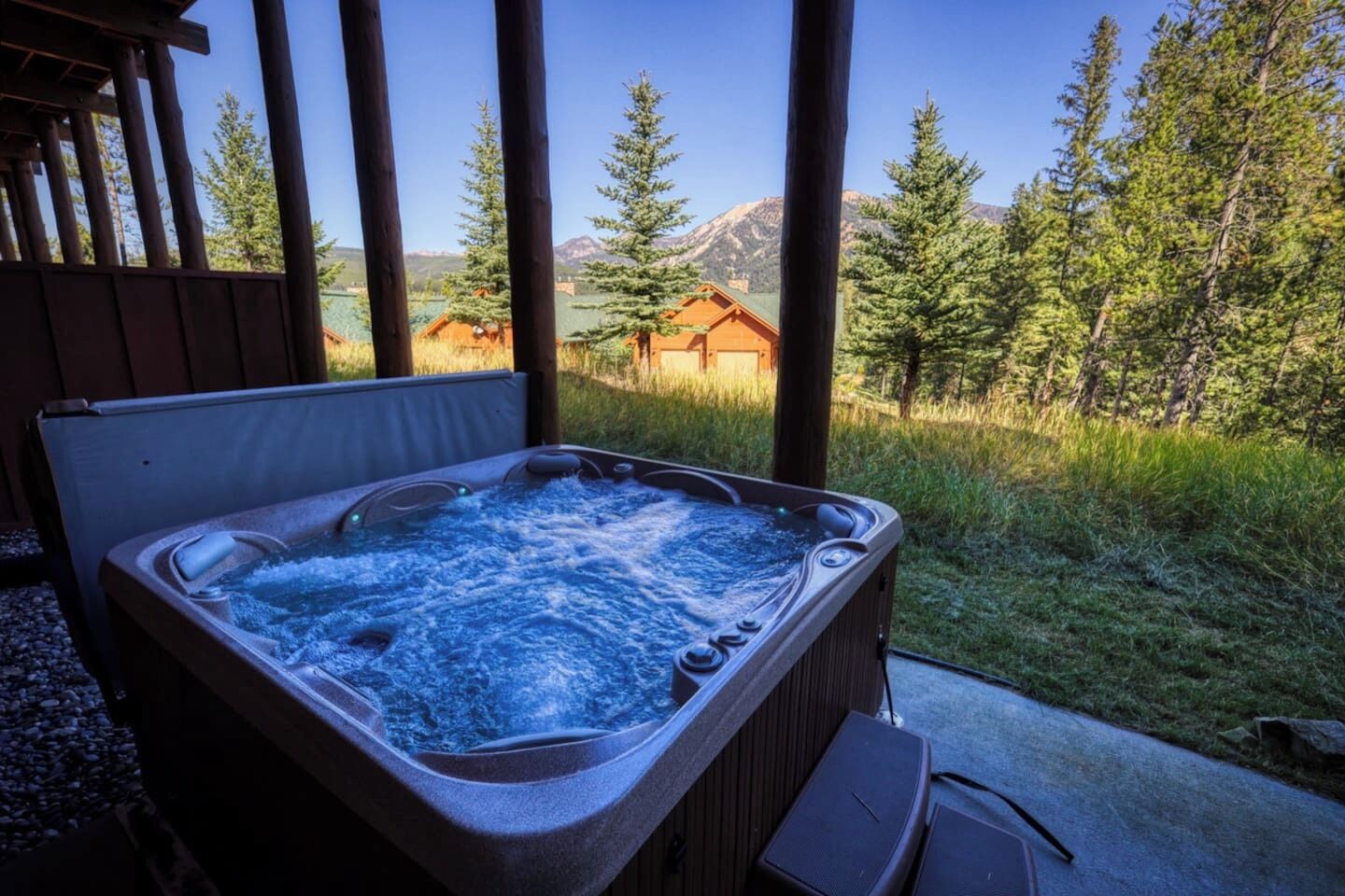 A hot tub with a wooden deck and a view of a mountain and forest.