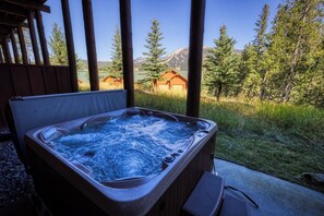 A hot tub with a wooden deck and a view of a mountain and forest.