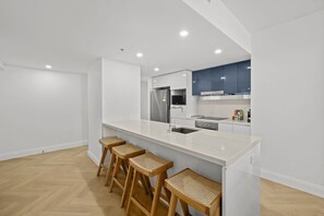 Eine moderne Küche mit weißer Arbeitsplatte, Edelstahlgeräten und Holzbarhocker.