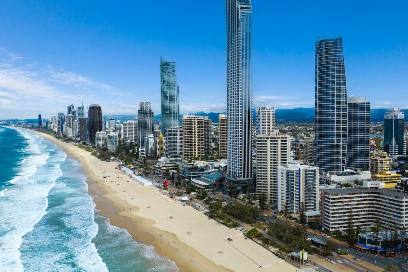 Un paisaje urbano costero con rascacielos, una playa arenosa y un cielo azul despejado.