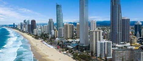 A coastal cityscape with high-rise buildings, a sandy beach, and a clear blue sky.
