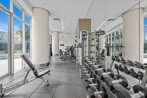A gym with exercise equipment, large windows, and a view of the city. - Luxurious 2BD Ocean View w/ Pool, Gym, Spa & Sauna (Surfers Paradise)