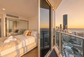 A bedroom with a large bed, a glass balcony, and a city view. - Luxurious 2BD Ocean View w/ Pool, Gym, Spa & Sauna (Surfers Paradise)