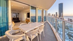 A balcony with a dining table and chairs, a sofa, and a city view. - Luxurious 2BD Ocean View w/ Pool, Gym, Spa & Sauna (Surfers Paradise)