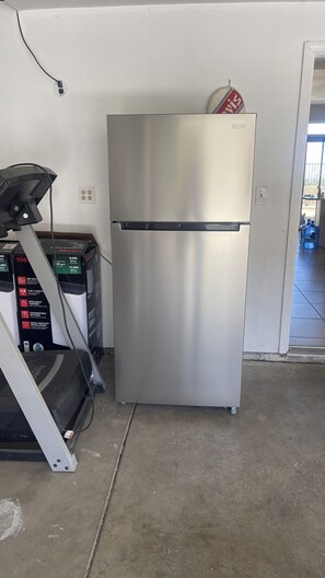 A stainless steel refrigerator in a room with a concrete floor, a treadmill, and a water dispenser. - Spacious 4BR Palmdale Home with Valley Views, Gym & Fireplace (Palmdale)