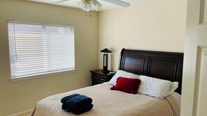 A bedroom with a bed, a nightstand, a lamp, and a window with blinds. - Spacious 4BR Palmdale Home with Valley Views, Gym & Fireplace (Palmdale)