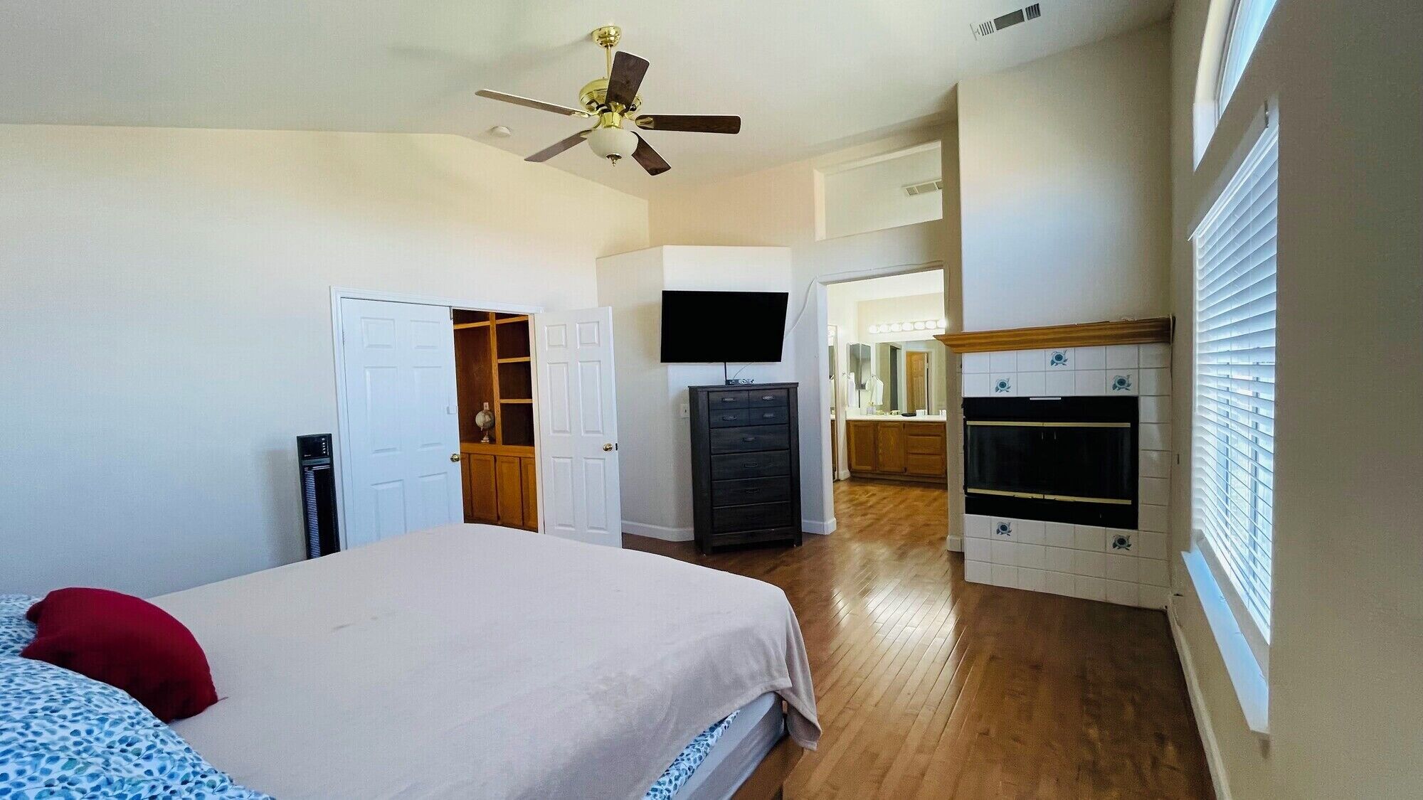 A bedroom with a bed, a TV, a dresser, and a ceiling fan.