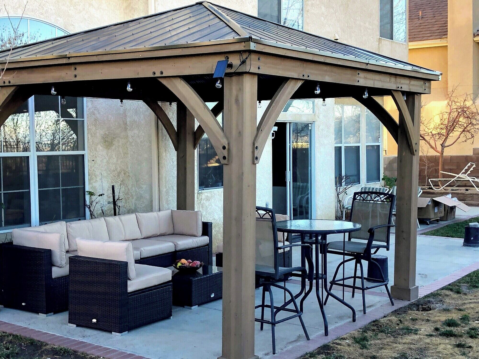 Un espace extérieur aménagé avec une zone salon couverte, comprenant un canapé et des fauteuils, une table et une structure en forme de pergola.