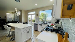 A modern kitchen with white cabinetry, a central island, a stove, and a dishwasher. - Spacious 4BR Palmdale Home with Valley Views, Gym & Fireplace (Palmdale)