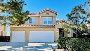 A two-story house with a red-tiled roof, two garage doors, and a small window on the upper floor. - Spacious 4BR Palmdale Home with Valley Views, Gym & Fireplace (Palmdale)