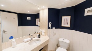 Et badeværelse med en hvid vask, et spejl, et toilet og en hårtørrer på væggen.