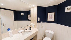 Un baño con un lavamanos blanco, un espejo, un inodoro y un secador de pelo en la pared.