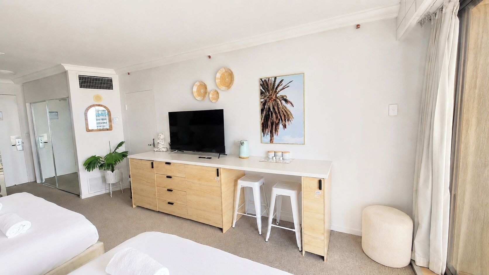 A hotel room with a bed, a desk with a TV, a mirror, and a plant.