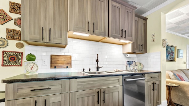 A kitchen with wooden cabinets, a stainless steel dishwasher, and a white tiled backsplash.