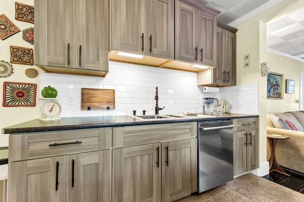 A kitchen with wooden cabinets, a stainless steel dishwasher, and a white tiled backsplash.