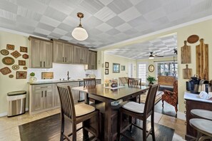 A spacious kitchen with wooden cabinets, a dining table, and chairs. There is a ceiling fan, a light fixture, and a view into the dining area.