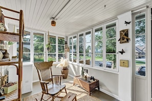 A sunroom with large windows, wicker furniture, and decorative items.