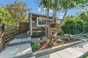 A modern house with a wooden exterior, a front porch, and a garden with various plants and a hanging flower basket.