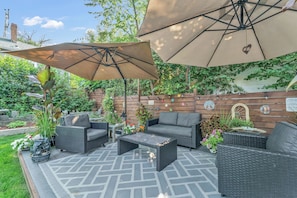 An outdoor patio with wicker furniture, a table, and two large umbrellas providing shade.