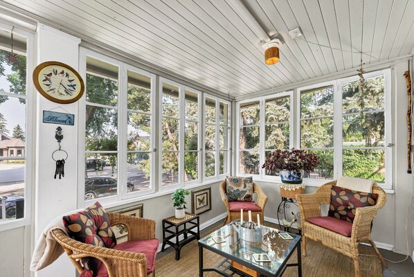 A sunroom with wicker furniture, a glass coffee table, and a view of trees and a street.