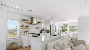Una cucina moderna con mobili bianchi, un'isola centrale e una zona pranzo con un divano bianco.