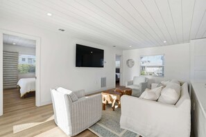 A spacious living area with a large flat-screen TV mounted on the wall, a striped sofa, a wooden coffee table, and a patterned rug. - Sandy Smiles - Gulf View 1-Min-Beach - Heated Pool (Fort Myers Beach)