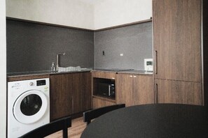 A compact kitchen with a washing machine, microwave, and dark wooden cabinets. - Imrang Stay Jungang (Busan)