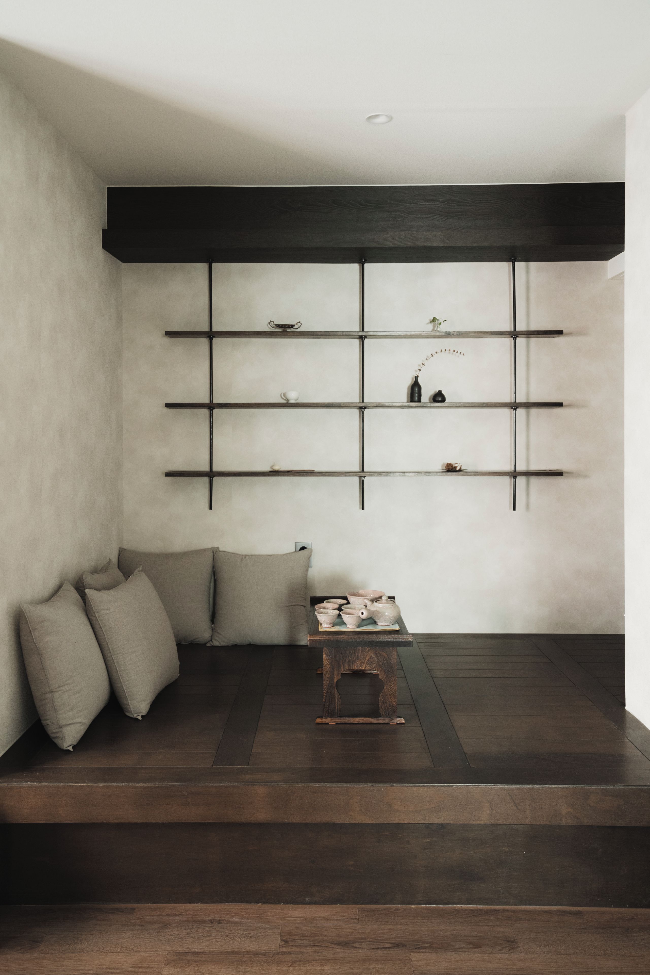 A room with a dark wooden floor, a low wooden bench, and a wall-mounted shelf with decorative items.