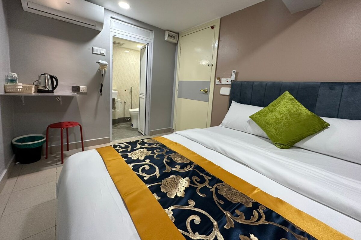 Una camera d'albergo con un letto, un comodino, una sedia rossa, uno specchio e l'accesso al bagno.