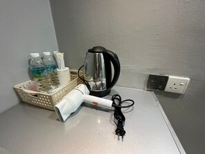 Una encimera de cocina con un hervidor, un secador de pelo y una cesta con agua embotellada y un pañuelo.