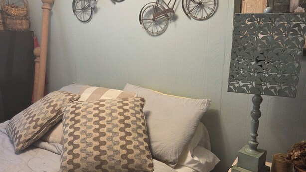 A bedroom with a bed, pillows, a nightstand, a lamp, and wall decorations including two bicycles.