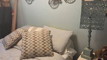 A bedroom with a bed, pillows, a nightstand, a lamp, and wall decorations including two bicycles.