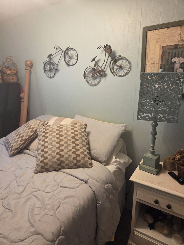 A bedroom with a bed, pillows, a nightstand, a lamp, and wall decorations including two bicycles.
