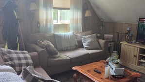A cozy loft-style living room with a high ceiling, a wooden coffee table, a sofa with cushions, a patterned rug, and a window with curtains.