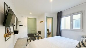 Ein Hotelzimmer mit einem Bett, einem an der Wand befestigten Fernseher, einem Schreibtisch mit Stuhl und einem fensterbepflanzten Fenster.
