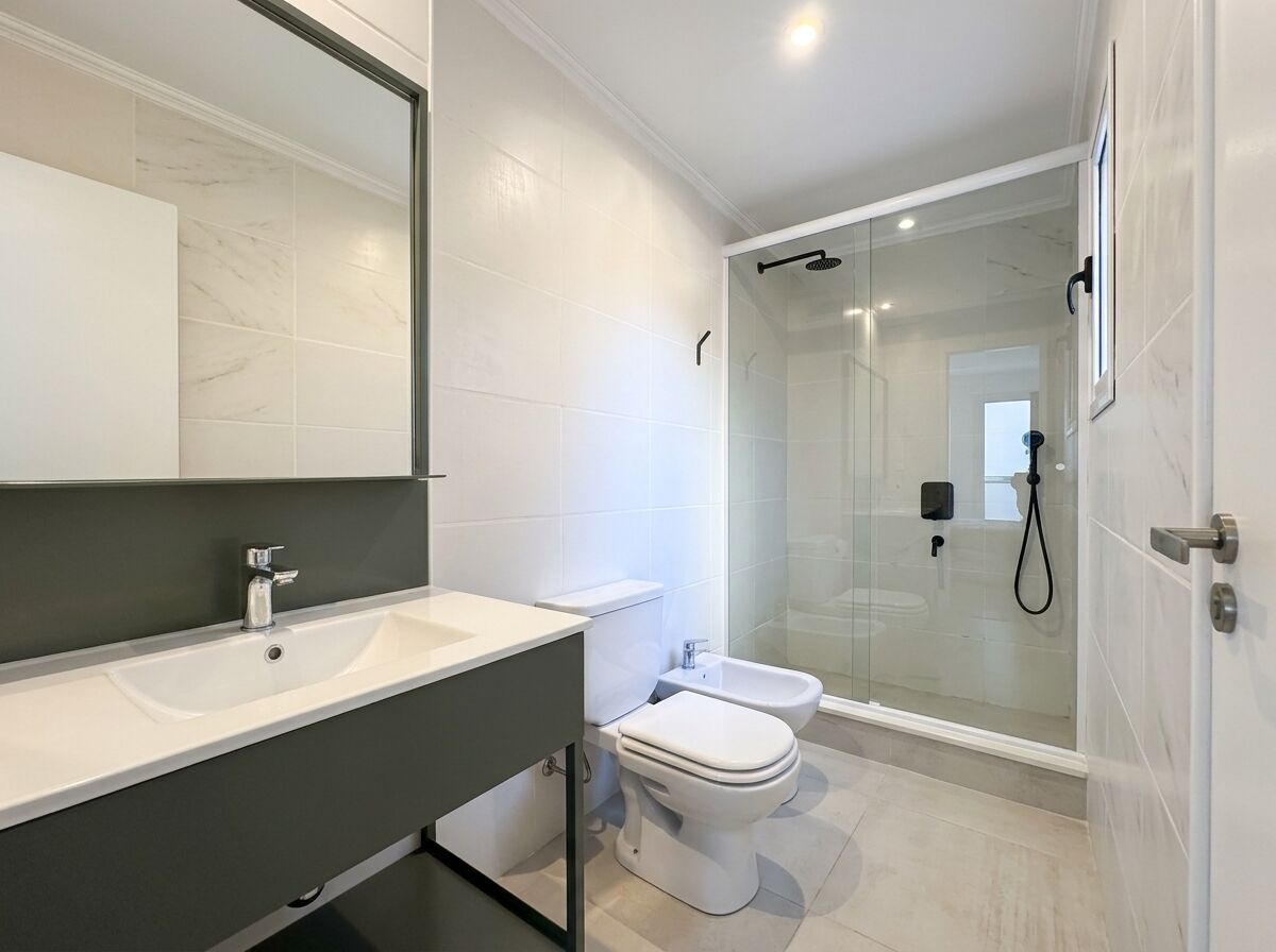 A modern bathroom with a large mirror, a white sink, a toilet, and a glass-enclosed shower area.