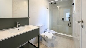 Ein modernes Badezimmer mit einem großen Spiegel, einem weißen Waschbecken, einer Toilette und einer Duschkabine.