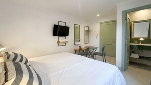 Ein Hotelzimmer mit Bett, Wandfernseher, Schreibtisch mit Stühlen sowie Bad mit Spiegel und Waschbecken.
