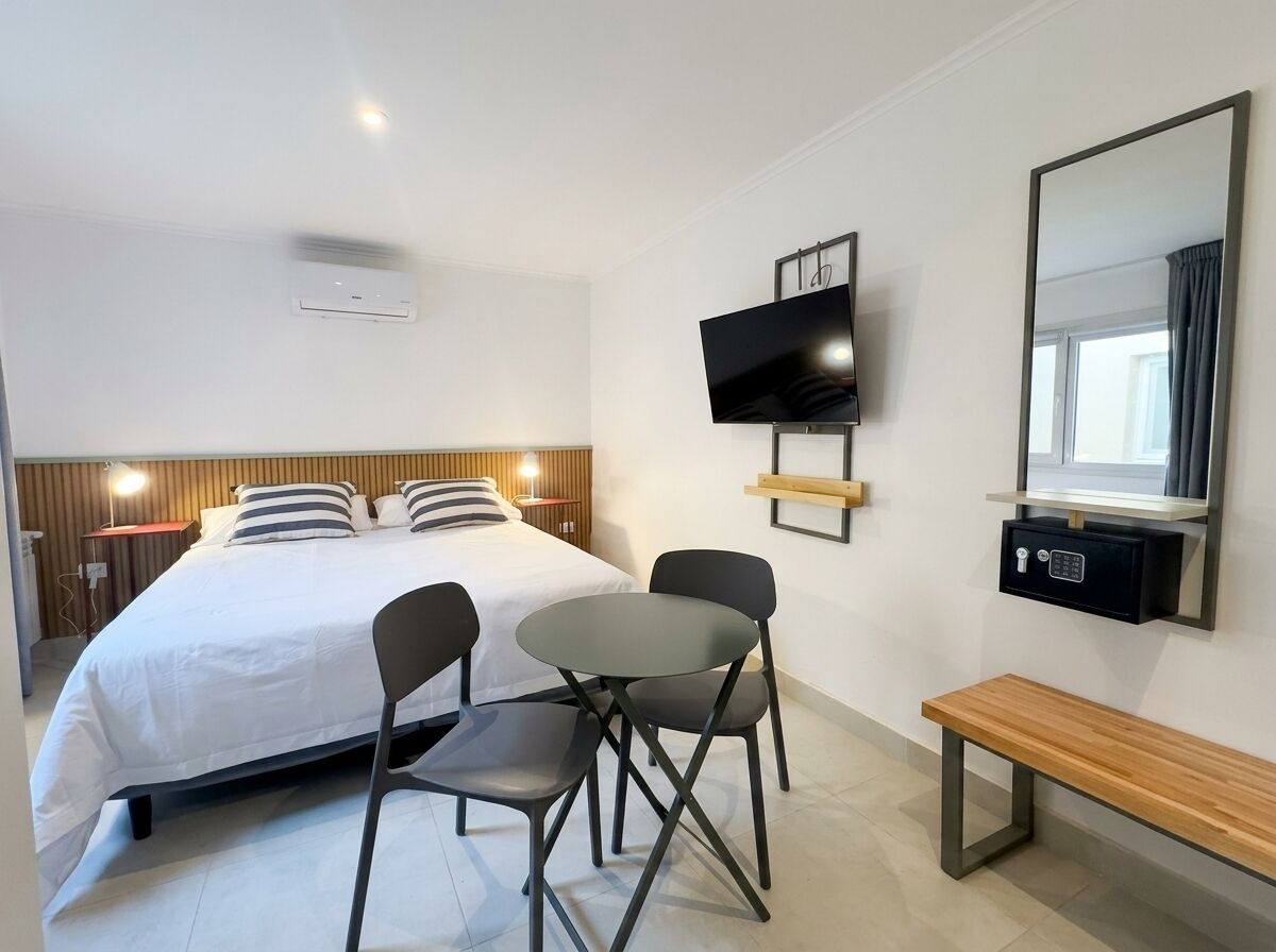 Una habitación de hotel moderna con cama, mesita de noche, televisor y una banca.