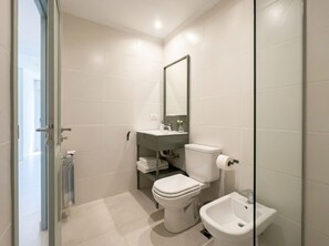 A modern bathroom with a toilet, bidet, and a glass shower enclosure.