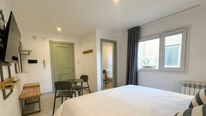 Ein Hotelzimmer mit einem Bett, einem Schreibtisch, einem Sessel, einem Fernseher, einer Tür und einem Fenster.