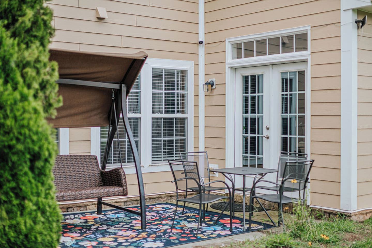 A patio with a swing chair, a table with chairs, and a decorative rug.