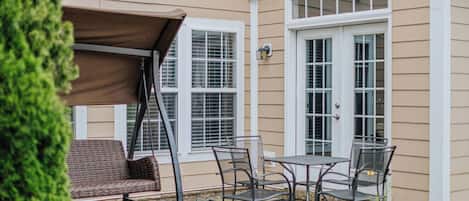 A patio with a swing chair, a table with chairs, and a decorative rug.