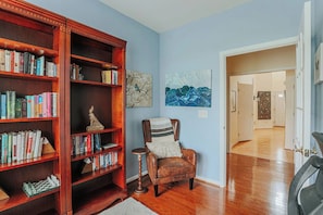 Una habitación con una estantería de madera, una silla y obras de arte en la pared.