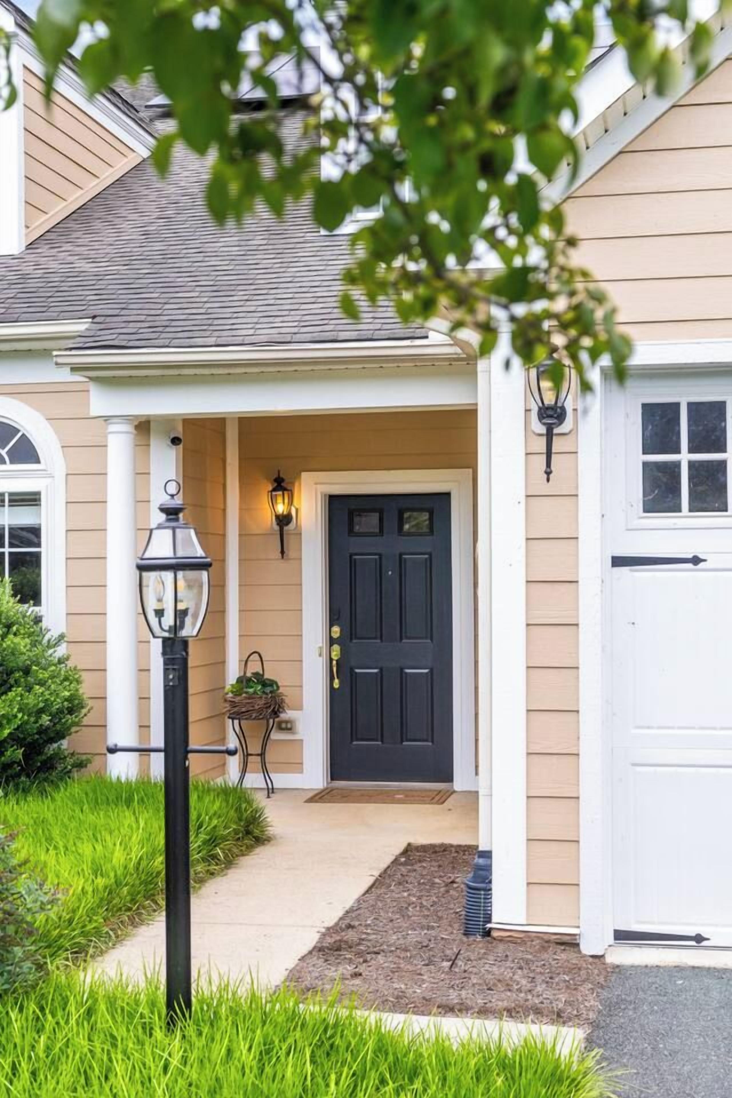 A house with a dark front door, a porch with a light fixture, and a small garden area.