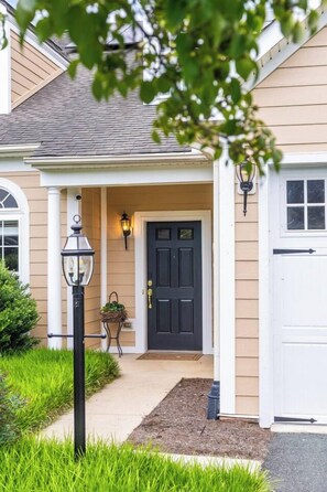 Uma casa com porta frontal escura, varanda com luminária e pequeno jardim.
