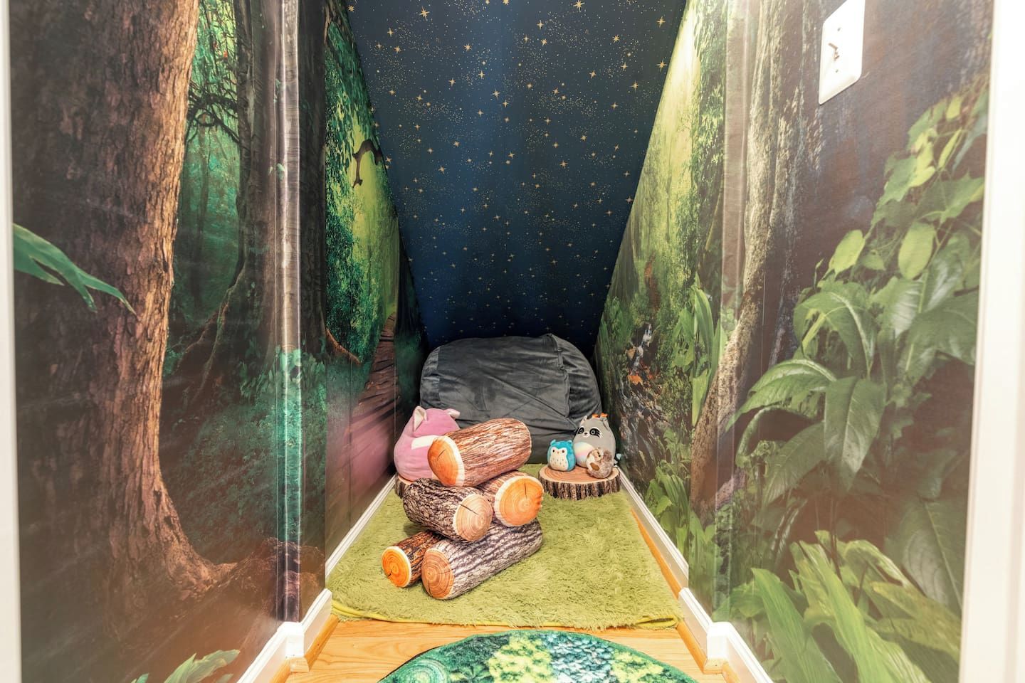 Une pièce chaleureuse avec une fresque murale sur le thème de la forêt, un lit, un tapis vert et une petite table avec des jouets.