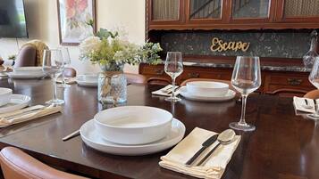 Une table à manger dressée avec des assiettes, des verres et des couverts, un vase rempli de fleurs et un buffet sur lequel est posée une pancarte.