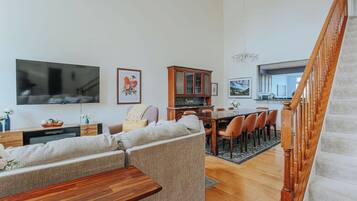 A living room with a sofa, a wooden coffee table, a TV, and a dining area with chairs and a table.