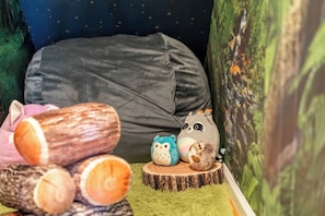Una habitación acogedora con una cama, una pared verde con un diseño de estrellas y una pequeña mesa de madera con juguetes suaves.